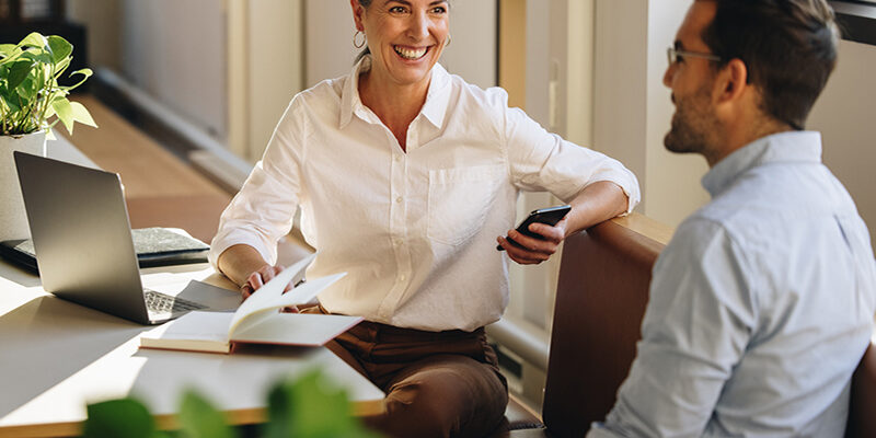 Businesswoman sitting at desk and explaining new project to coworker. Mature woman discussing working with partner in coworking office.