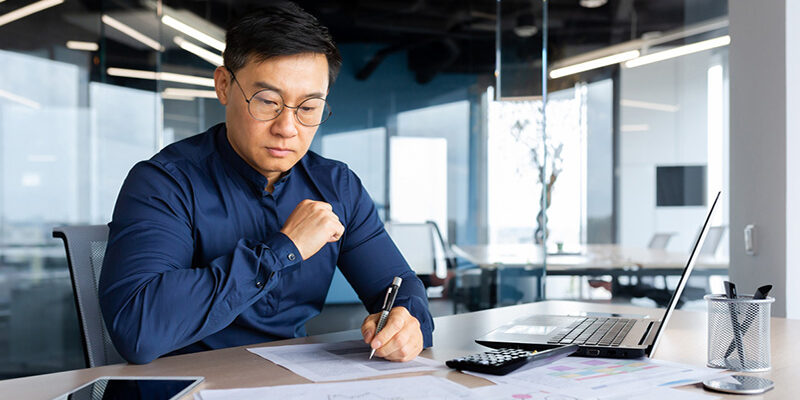 Serious thinking asian man working with documents inside office, concentrated businessman with contracts and bills reading and calculating reports, mature financier with documents.